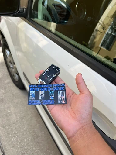 A technician's hand holding a new car key fob and a business card for Local Locksmith Pros LLC, representing their expert Automotive Locksmith Services.