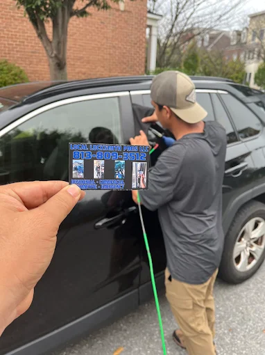 A technician from Local Locksmith Pros LLC performing a car lockout service, showcasing their professional Automotive Locksmith skills, with a business card held in the foreground.