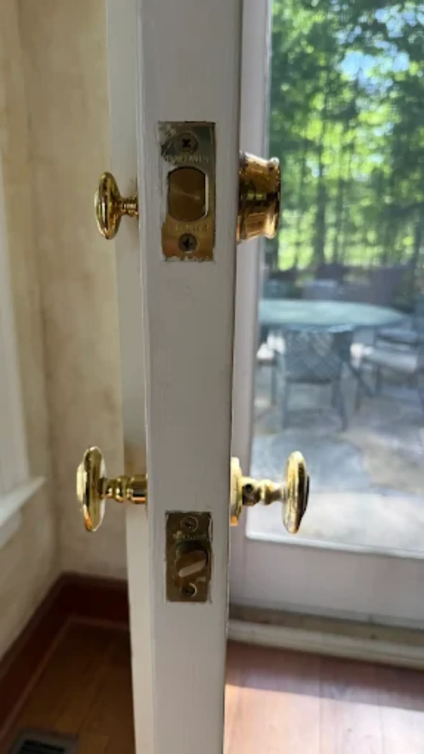 Residential Locksmith Services by Local Locksmith Pros LLC, featuring the side view of a white door equipped with a brass deadbolt and a matching doorknob, leading to an outdoor patio.