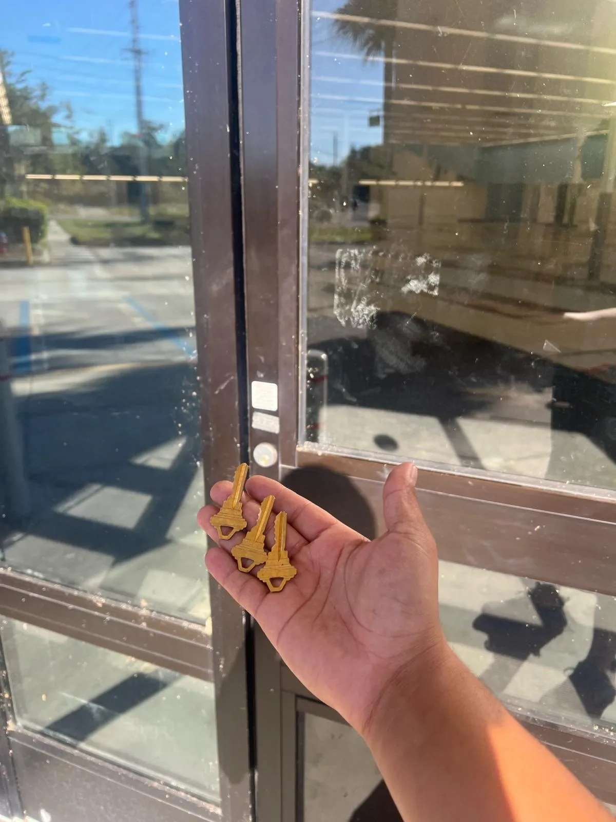 A technician from Local Locksmith Pros LLC holding three new keys after performing a Commercial Lock Rekeying service on a glass storefront door.