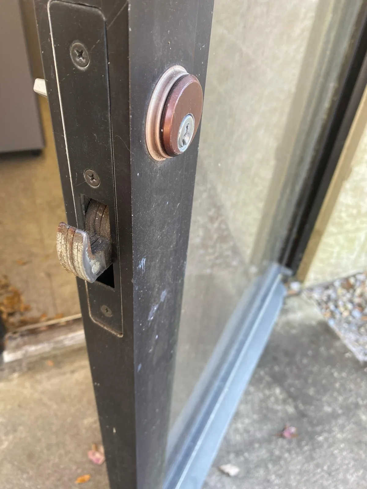A close-up of a worn hook bolt latch on a commercial storefront door, illustrating a common issue that requires Commercial Lock Repair by Local Locksmith Pros LLC.