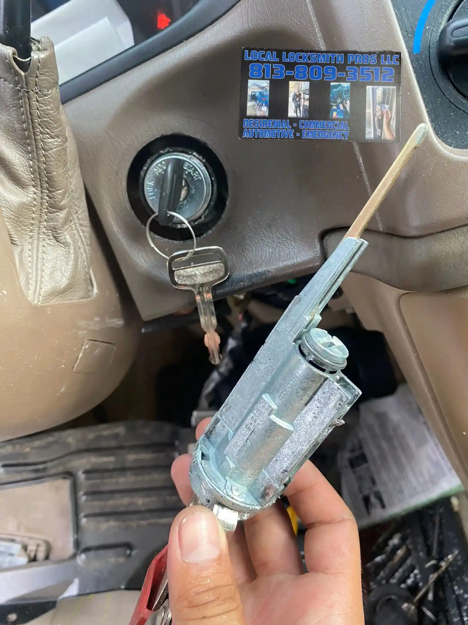 A technician from Local Locksmith Pros LLC performing Ignition Repair Services, holding a removed ignition lock cylinder for detailed work, with the car's steering column visible.