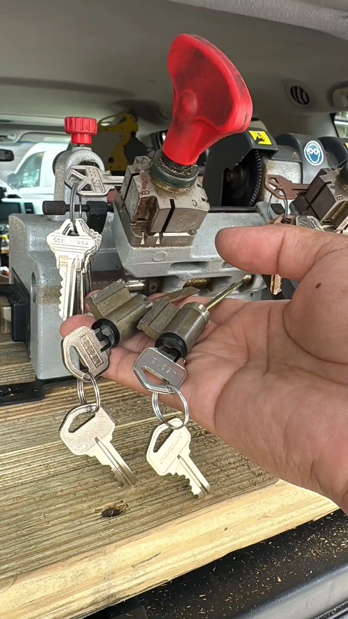 A technician from Local Locksmith Pros LLC holding two new automotive ignition lock cylinders, demonstrating professional Ignition Replacement Services with a key cutting machine in the background.
