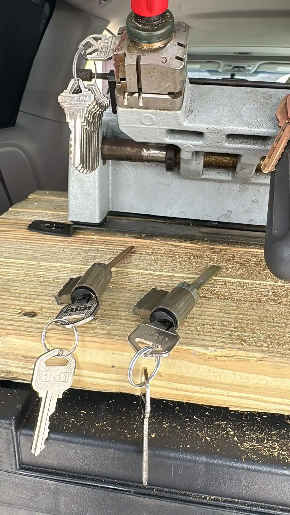 Ignition Replacement Services by Local Locksmith Pros LLC, featuring two vehicle ignition lock cylinders with keys, set on a workbench with a key cutting machine in the background.