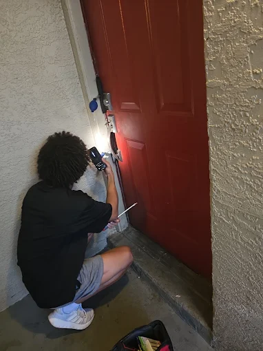A technician from Local Locksmith Pros LLC performing a Lock Rekeying service on a red residential door, using a flashlight to illuminate the lock.