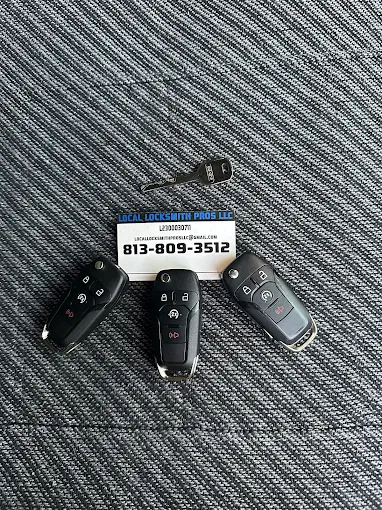 Automotive Locksmith Services by Local Locksmith Pros LLC, featuring three new car key fobs and a cut key displayed with the company's business card on a textured surface.