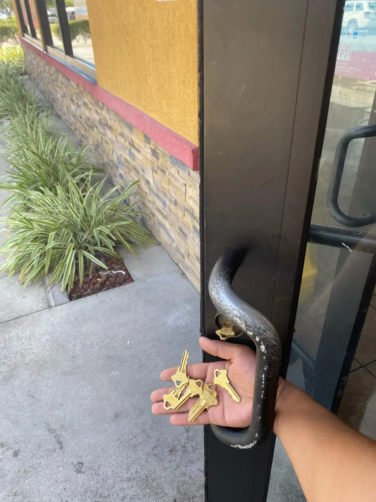 A technician from Local Locksmith Pros LLC holding a handful of new brass keys next to a commercial glass door, showcasing a completed Commercial Lock Rekeying service.