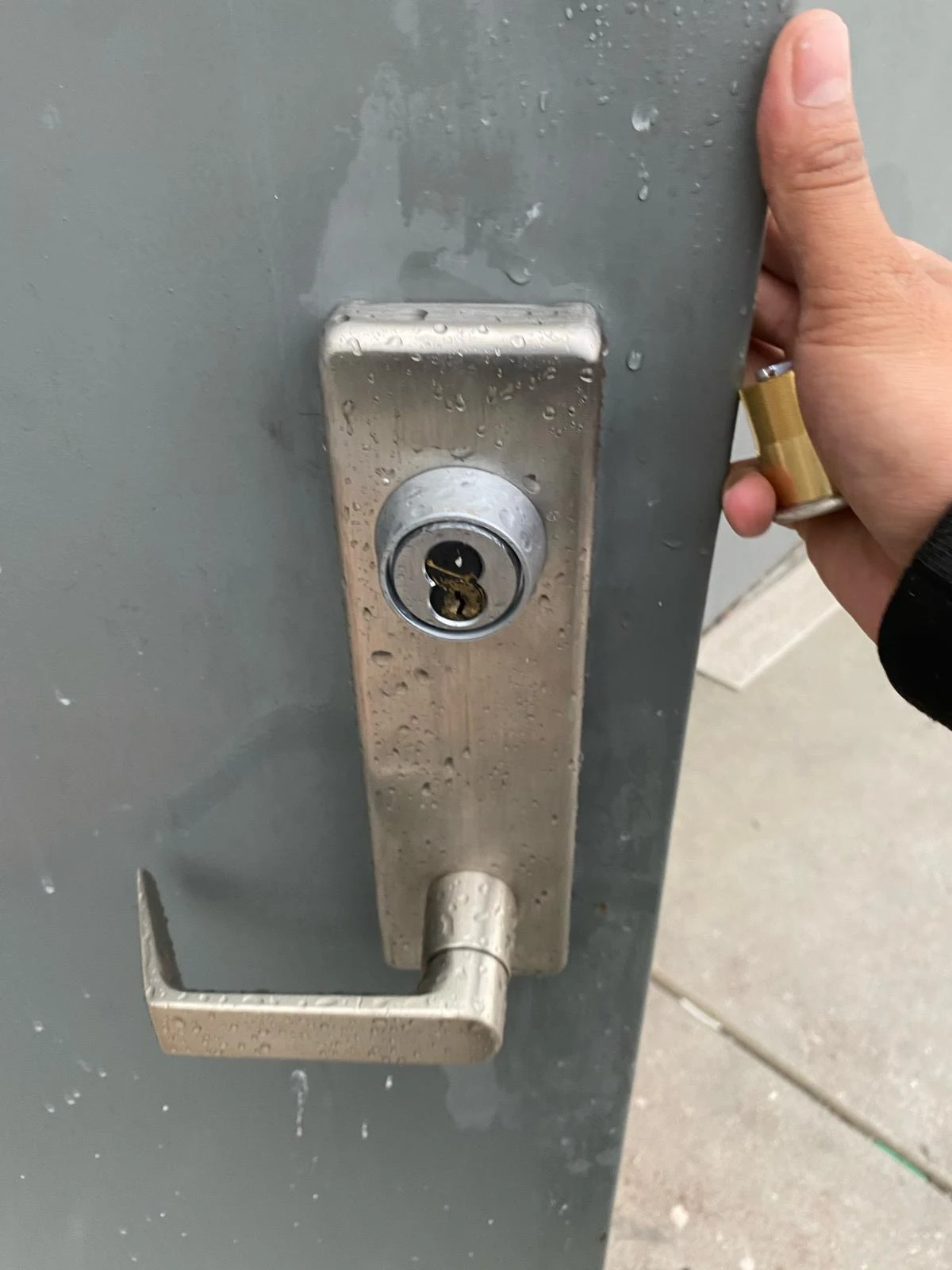 A technician from Local Locksmith Pros LLC performing Commercial Lock Repair, holding a lock cylinder next to a heavy-duty door handle with its core removed.