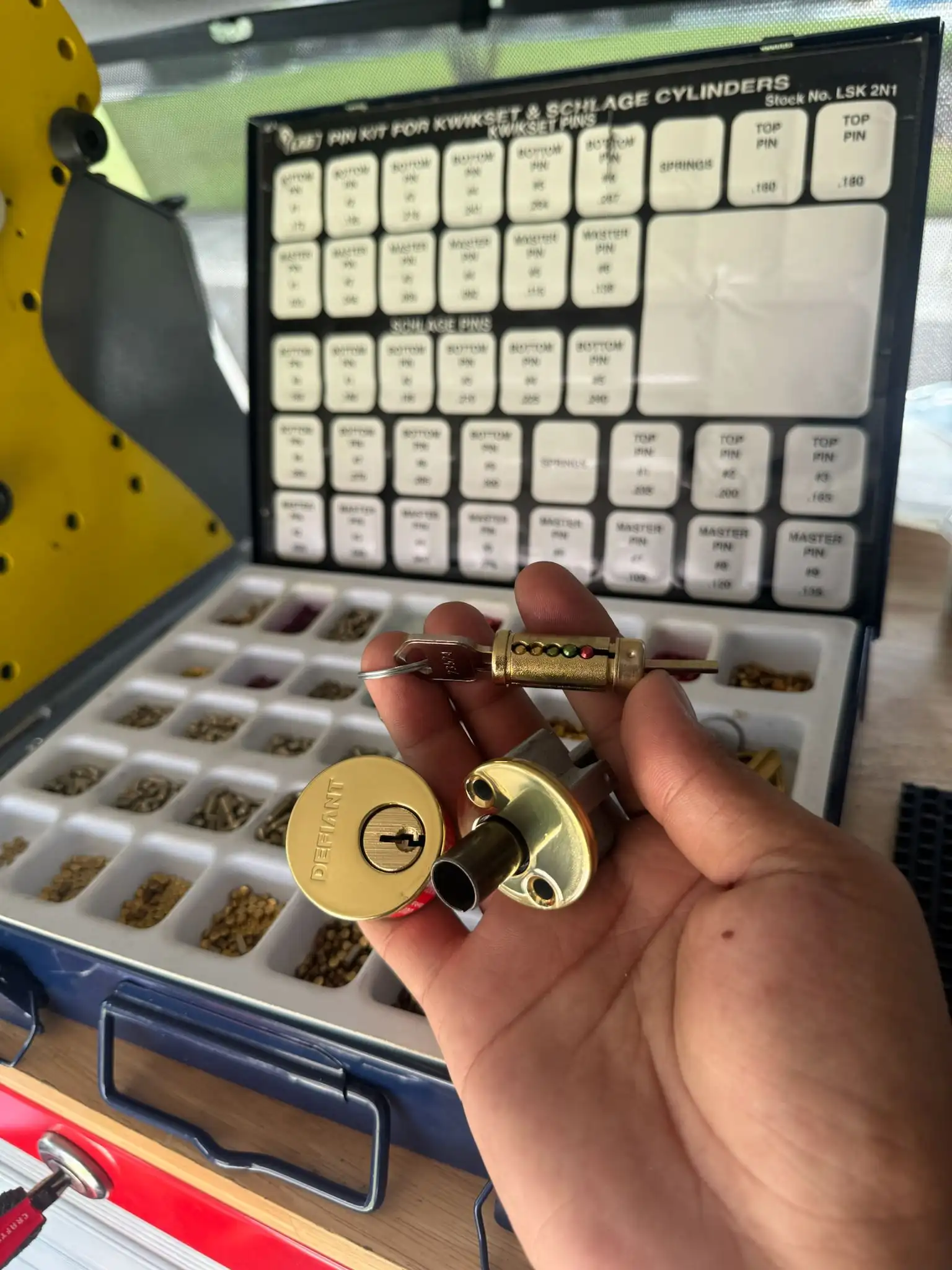 Professional Locksmith Services by Local Locksmith Pros LLC, showcasing a technician's hand holding a lock cylinder and a re-pinned core in front of a master pinning kit.