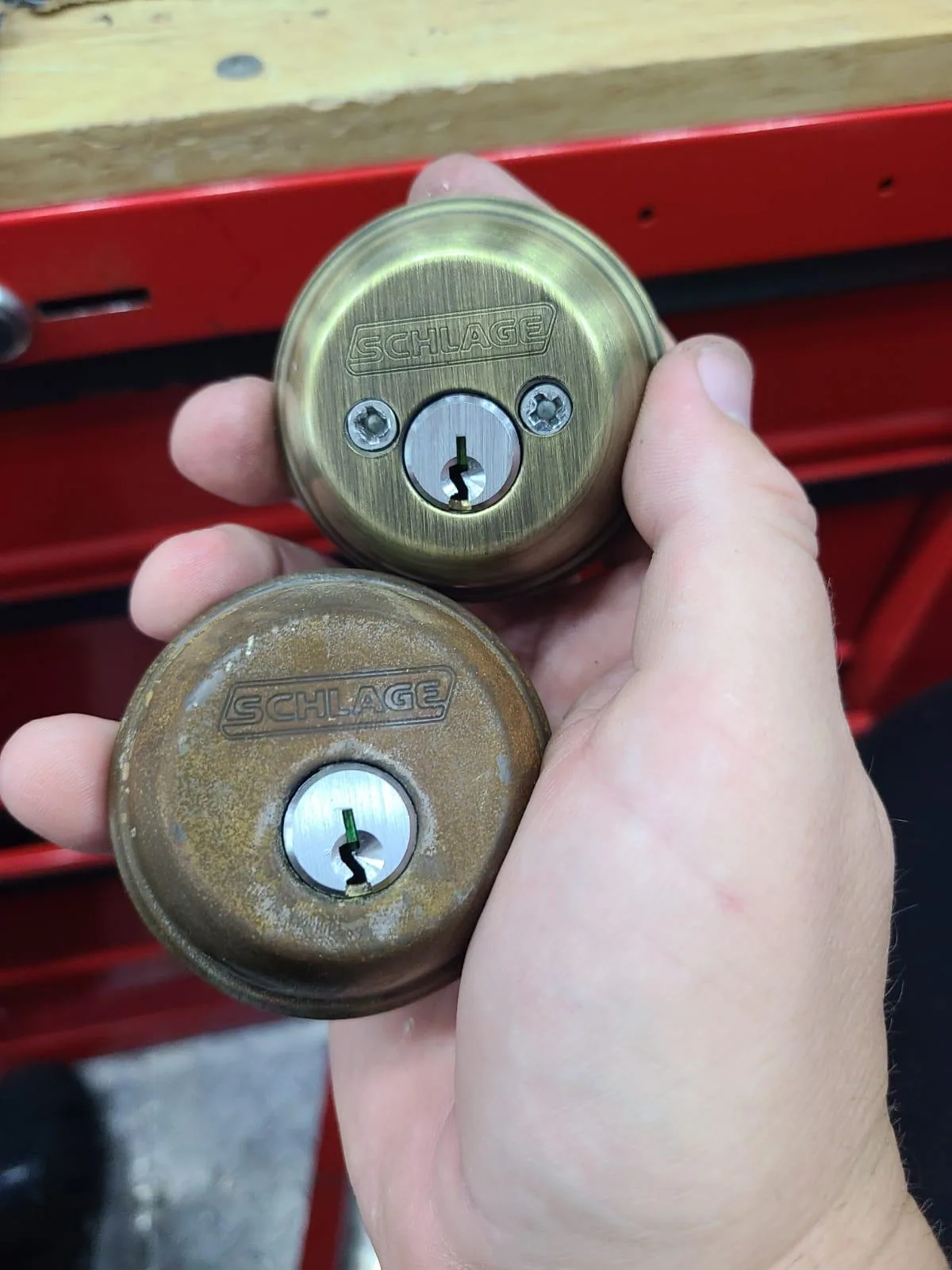 A Residential Locksmith from Local Locksmith Pros LLC holding a new and an old Schlage deadbolt, demonstrating a lock replacement or upgrade service.