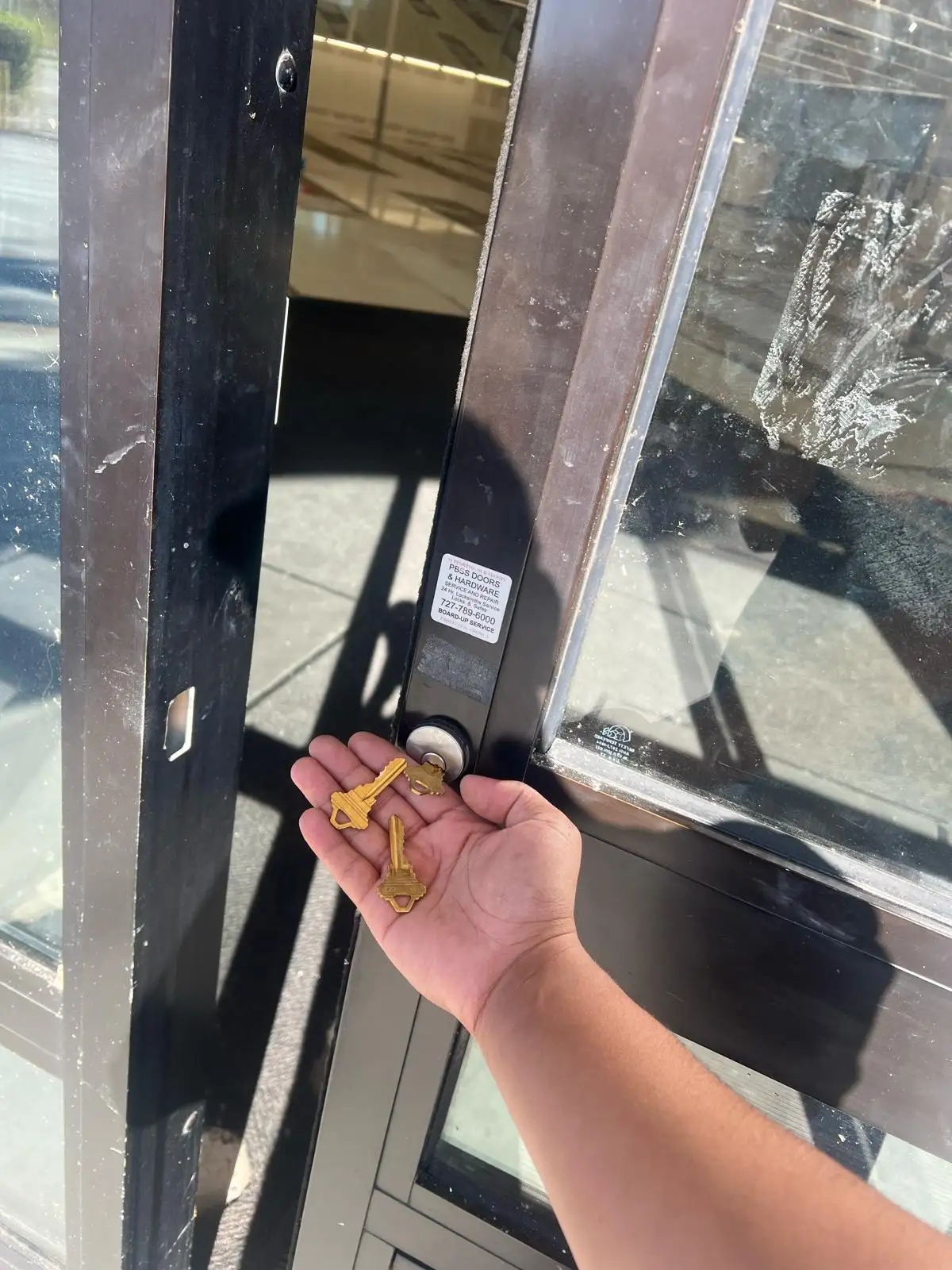 A technician from Local Locksmith Pros LLC holding three new keys in front of a glass storefront door, demonstrating a successful Commercial Lock Rekeying.