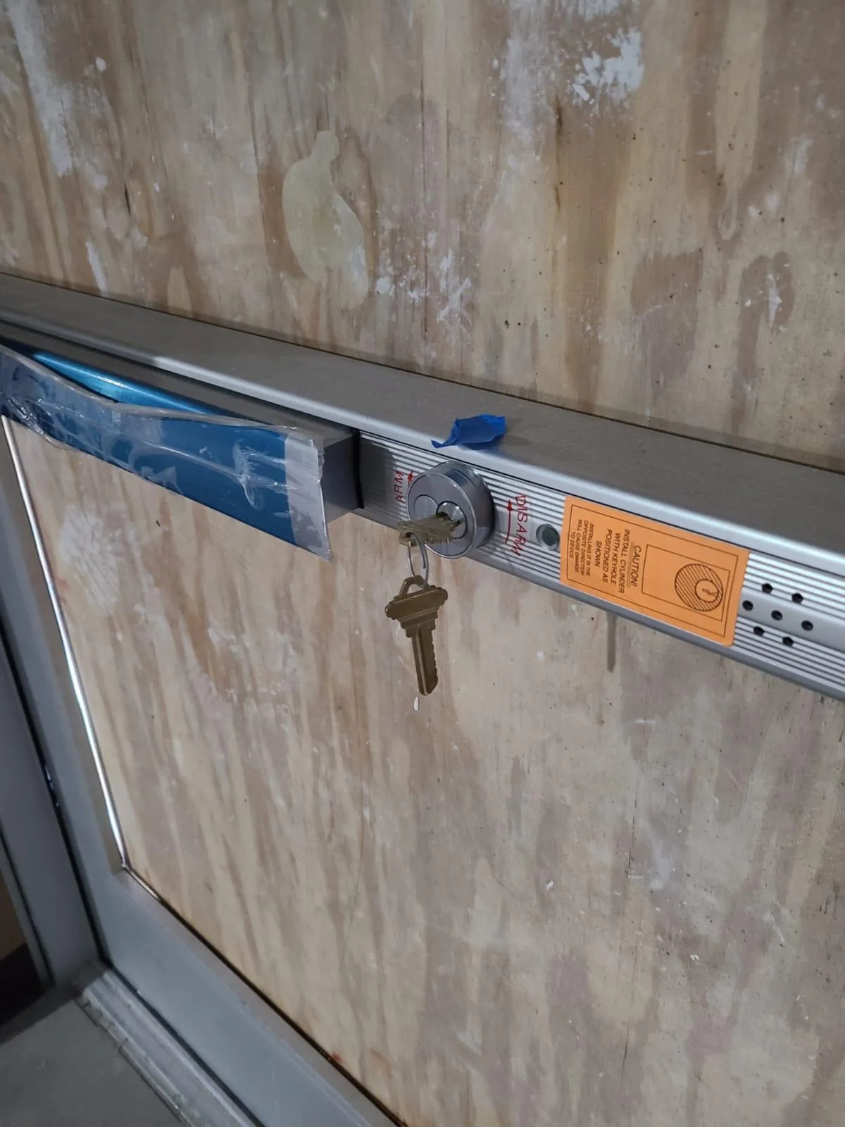 A Commercial Locksmith from Local Locksmith Pros LLC installing or repairing a panic bar exit device on a business door, with a key in the new lock cylinder.